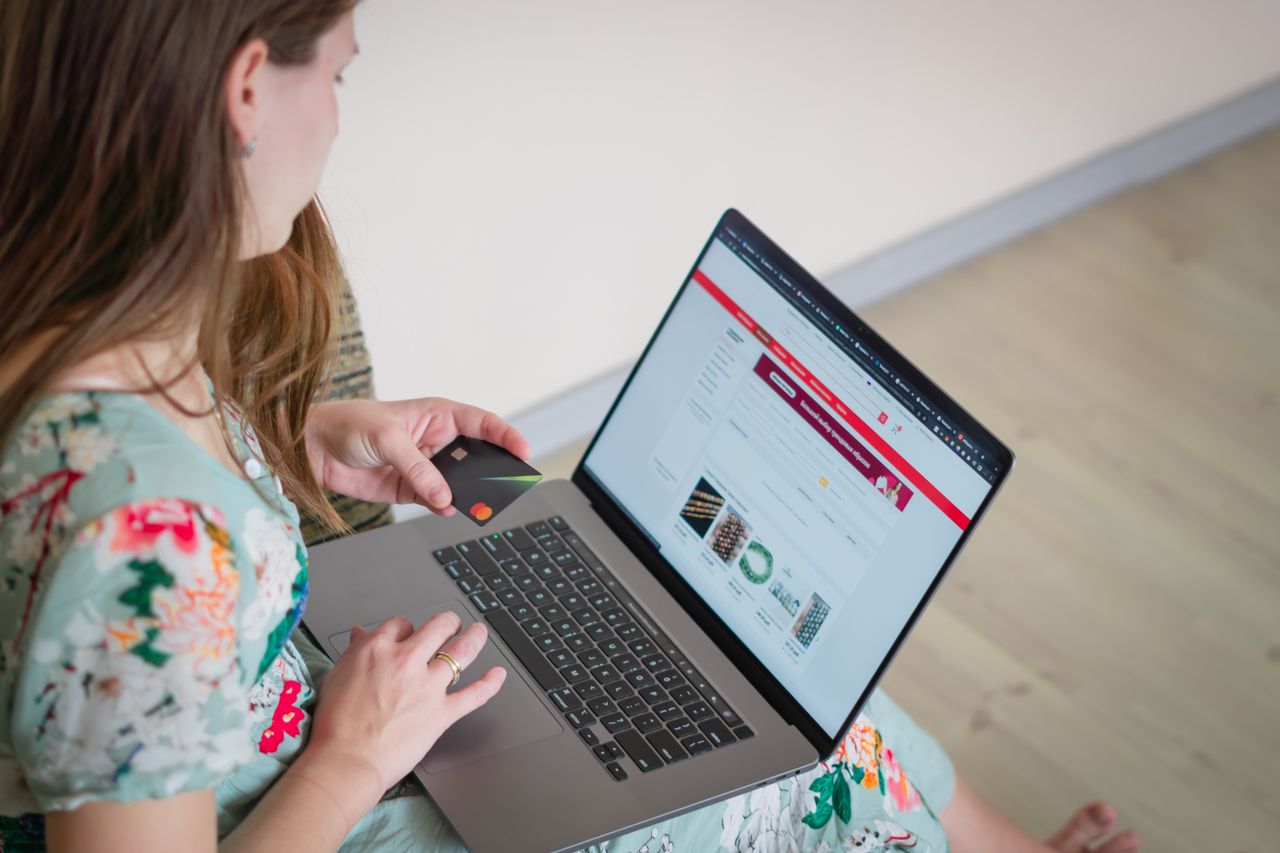 about-01 Woman in floral dress shopping online with a laptop and credit card indoors.